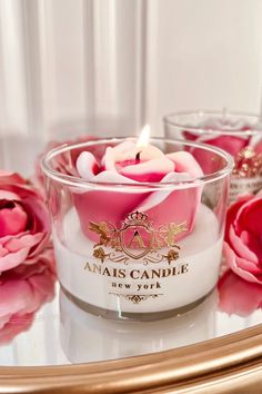 a candle that is sitting in a glass bowl on a table next to pink flowers