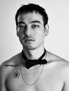 a shirtless man wearing a black bow tie with barbed wire around his neck and tattoos on his chest