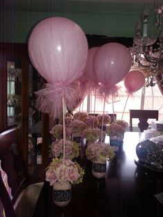 pink balloons and flowers in vases on a dining room table with chandelier