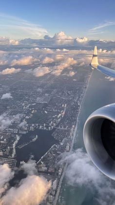 the wing of an airplane flying over clouds and water in the sky with city below