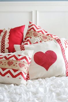 a white bed topped with lots of pillows and red hearts on it's covers