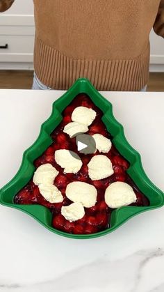 a person standing in front of a christmas tree shaped tray with fruit and cheese on it