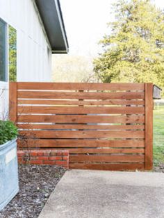 a wooden fence next to a house with potted plants on the side and grass in front