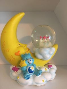 a toy bear sitting on top of a cloud next to a crystal ball in the shape of a moon