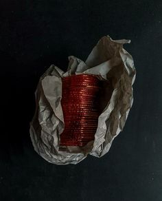 a roll of red wire sitting on top of a piece of paper next to a cup