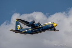 a blue and yellow airplane flying in the sky with white clouds behind it on a sunny day