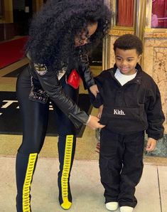 a little boy standing next to a woman in black and yellow boots on the sidewalk