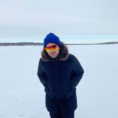 a man standing in the snow wearing sunglasses and a blue jacket with a fur collar