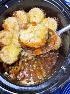 a crock pot filled with stew and biscuits being spooned into the casserole