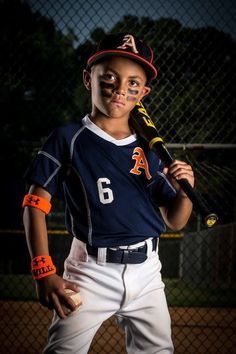 a young boy holding a baseball bat on top of a field at night with his face painted