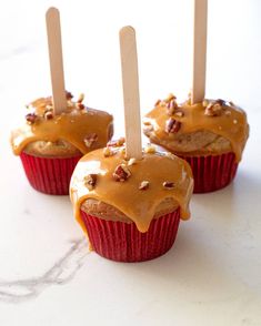 three cupcakes covered in caramel icing and topped with wooden stick sticking out of them