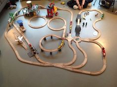 a child sitting on the floor next to a toy train set with cars and tracks