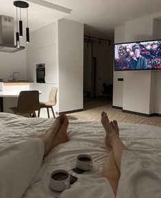 two people laying on a bed with their feet propped up in front of the tv