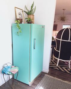 a blue refrigerator sitting in the corner of a room next to a chair and potted plant