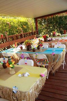 tables and chairs are set up on the deck for an outdoor party with flowers in vases