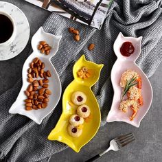 two plates with food on them next to a cup of coffee and saucer filled with almonds