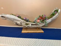 a piece of driftwood with succulents and flowers on it sitting on a table