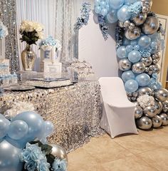 a table topped with blue and silver balloons next to a mirror filled with white flowers