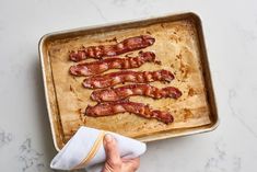 a person wiping up bacon on top of a baking pan