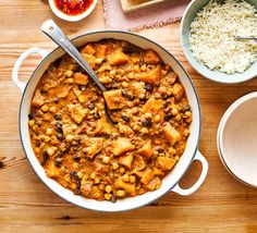 a pot filled with stew next to bowls of rice and other foods on a wooden table