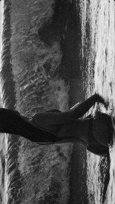 a woman standing on the beach with her arms spread out and feet in the water