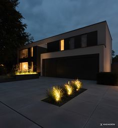 a modern house lit up at night with plants in the foreground and lights on