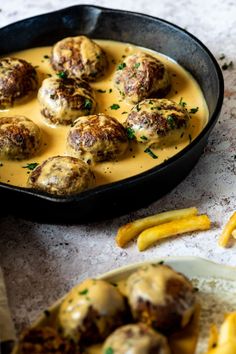 a pan filled with meatballs covered in sauce next to french fries on a table