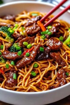 beef and broccoli lo mein in a white bowl with chopsticks on the side