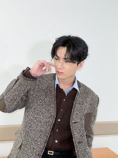 a man with glasses and a blazer is pointing to his left side while standing in front of a table