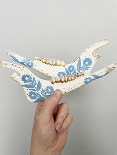 a hand holding a blue and white bird figurine with flowers on it's wings