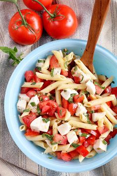 a blue bowl filled with pasta, tomatoes and fettuccine on top of a table