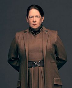 a woman in a brown coat is posing for a photo with her hands on her hips