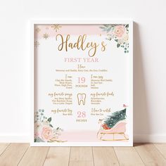 a pink and gold baby's first year print with flowers on the bottom, in front of a white wall