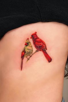 two birds sitting on the side of a woman's stomach, one red and one yellow