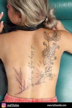 the back of a woman's body with flowers and words tattooed on her lower back