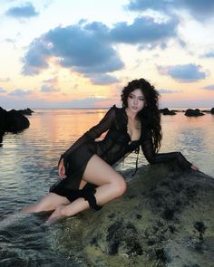 a woman sitting on top of a rock next to the ocean