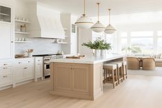 a large kitchen with white cabinets and wood flooring is pictured in this image, there are several stools on the island