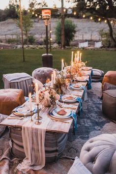 a table set up with candles and place settings for an outdoor dinner in the evening