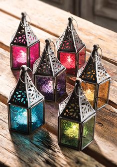 four colorful lanterns sitting on top of a wooden table next to each other with lights inside them