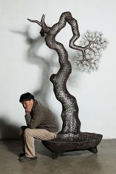 a man kneeling down next to a metal sculpture with a tree on it's side