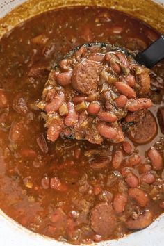 a spoon full of beans and sausage in a bowl