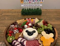 a wooden bowl filled with lots of different types of cheeses and fruit on top of a table