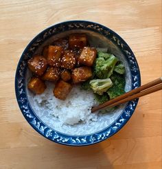 a bowl filled with rice, broccoli and meat next to chopsticks