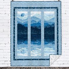 a quilted wall hanging on the side of a white brick building with mountains in the background