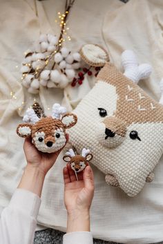 two knitted deer ornaments are being held up by someone's hands on a white blanket