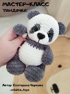 a hand holding a small stuffed animal in the shape of a panda bear with green eyes