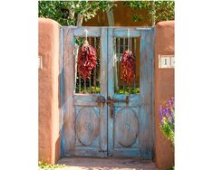 an old blue door with two red peppers hanging from it's sides and some purple flowers in the foreground