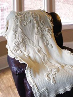 a white crocheted blanket sitting on top of a leather chair next to a window