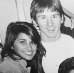 a black and white photo of a young man and woman smiling at the camera with their arms around each other