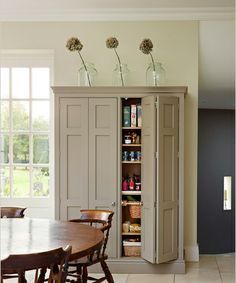 an open cabinet in the middle of a room next to a dining table and chairs